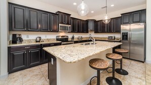 A modern kitchen with dark cabinets, a granite countertop, stainless steel appliances, and a central island with bar stools. - Grhbch2953 - Paradise Palms Resort - 6 Bed 5 Baths House (Kissimmee)