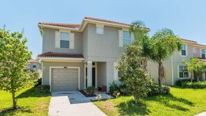 A two-story residential building with a red-tiled roof, a garage, and a well-maintained lawn with small trees. - Grhbch2953 - Paradise Palms Resort - 6 Bed 5 Baths House (Kissimmee)