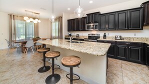A modern kitchen with dark cabinets, a granite countertop, and a central island with bar stools. - Grhbch2953 - Paradise Palms Resort - 6 Bed 5 Baths House (Kissimmee)