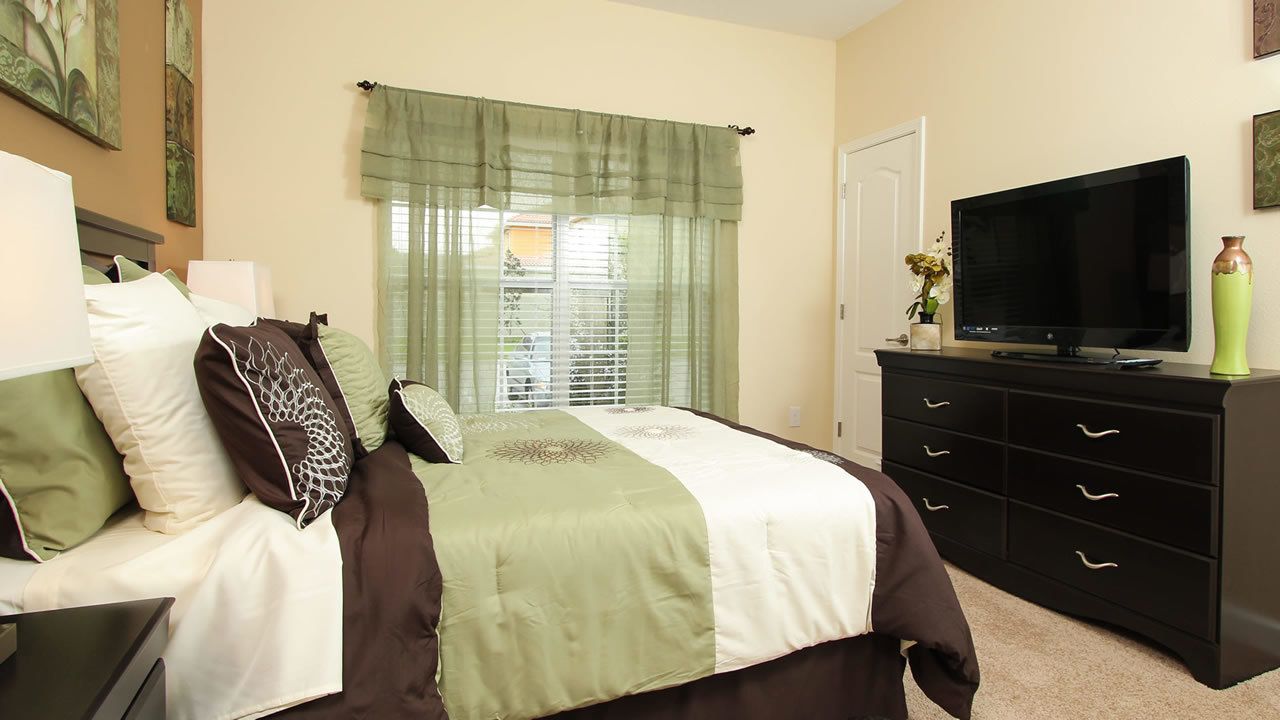 A bedroom with a bed, a TV, a dresser, and a window with curtains.
