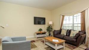 A living room with a sofa, armchair, coffee table, TV, and a window with curtains. - Grhbch3057 - Paradise Palms Resort - 5 Bed 4 Baths Townhouse (Kissimmee)