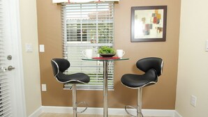 Une pièce comprenant deux tabourets de bar noirs, une petite table ronde avec un dessous de verre rouge et une plante en pot.