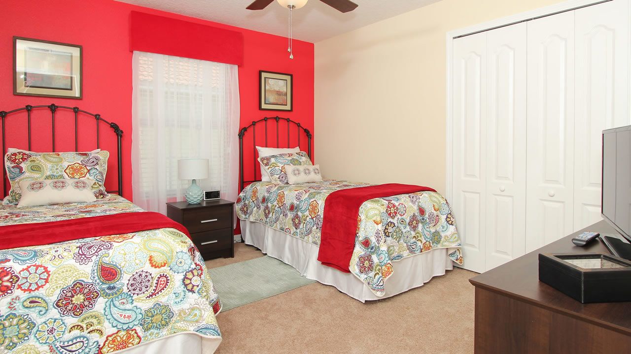 A bedroom with two beds, a nightstand, a dresser, and a ceiling fan.