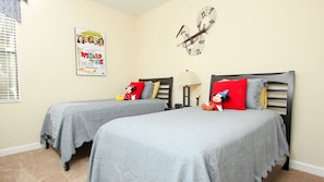 A bedroom with two beds, each with a Mickey Mouse pillow, a poster of 'Wizards of Oz' on the wall, and a clock.