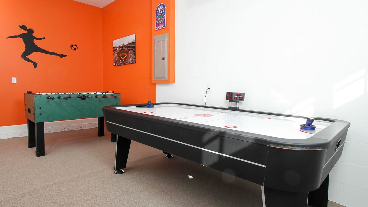 A room with a foosball table, a pool table, and a green sofa.