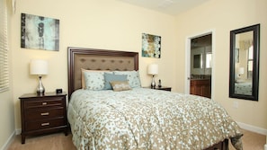 A bedroom with a large bed, two bedside tables, a nightstand, a mirror, and artwork on the walls.