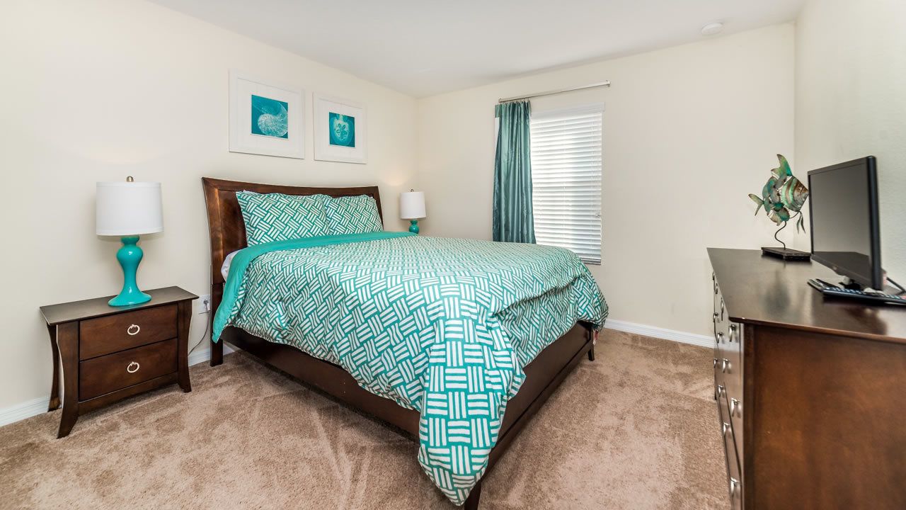 A bedroom with a bed, two bedside tables, a dresser, a television, and artwork on the wall.