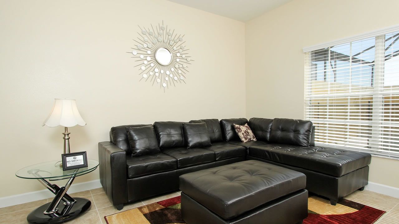 A living room with a sectional sofa, a glass coffee table, a lamp, and a decorative wall piece.