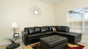 A living room with a sectional sofa, a glass coffee table, a lamp, and a decorative wall piece. - Grhmap8952 - Paradise Palms Resort - 4 Bed 3 Baths Townhouse (Kissimmee)