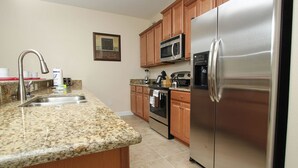 A kitchen with granite countertops, stainless steel appliances, wooden cabinets, and a microwave above the oven.