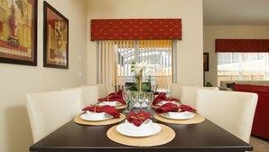 A dining table set for four with white plates, red napkins, and a vase of flowers.