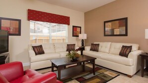 A living room with two white sofas, a red chair, a dark wooden coffee table, and a window with blinds.