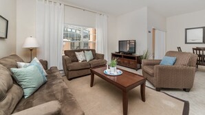 A living room with a brown sofa, a patterned armchair, a wooden coffee table, and a television on a wooden stand. - Grhcat8968 - Paradise Palms Resort - 4 Bed 3 Baths Townhouse (Kissimmee)