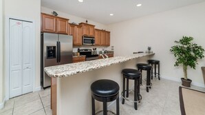 A modern kitchen with a central island, stainless steel appliances, wooden cabinets, and a potted plant. - Grhcat8968 - Paradise Palms Resort - 4 Bed 3 Baths Townhouse (Kissimmee)