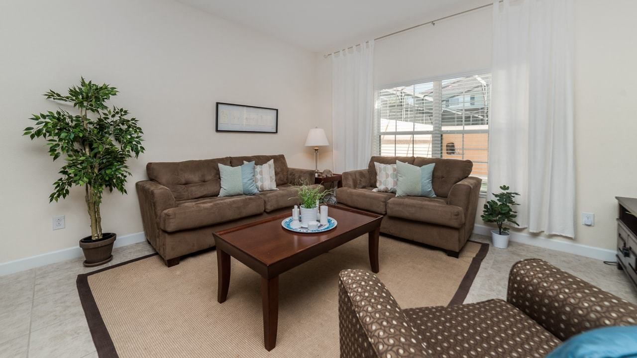 A living room with two brown sofas, a coffee table, a patterned armchair, and a potted plant.
