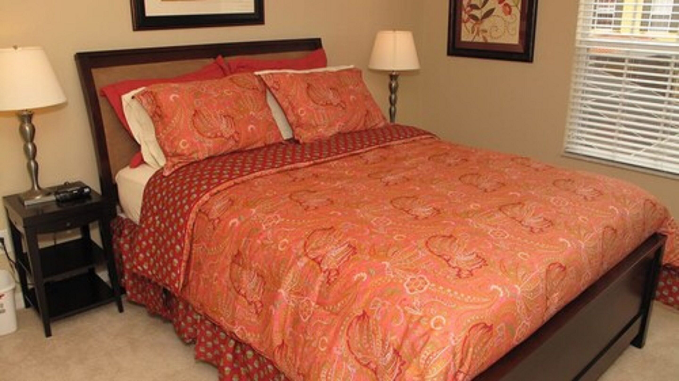 Uma cama bem arrumada com um cobreleito estampado, duas luminárias de cabeceira e um quadro na parede.