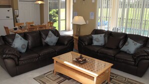 A living room with two brown leather sofas, a glass coffee table, and a dining area with wooden chairs and a table. - Grhlic2691 - Emerald Island Resort - 7 Bed 5 Baths House (Kissimmee)