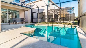 A modern outdoor swimming pool with a glass enclosure, a patio area with chairs, and a view of a building with large windows. - Grhbis8974 - Paradise Palms Resort - 5 Bed 5 Baths House (Kissimmee)