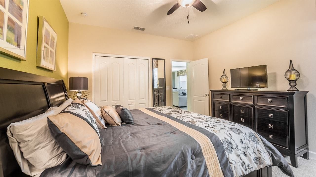 A bedroom with a bed, dresser, TV, and a ceiling fan.