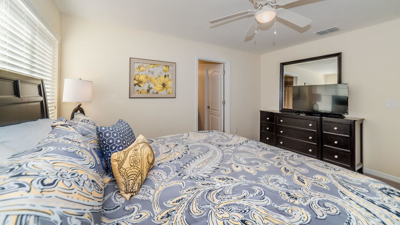 A bedroom with a bed, a dresser, a television, and a ceiling fan.