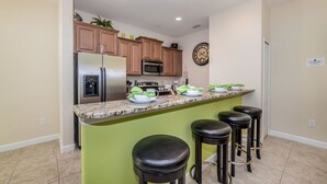 Una cocina con una isla central, electrodomésticos de acero inoxidable y taburetes de bar.