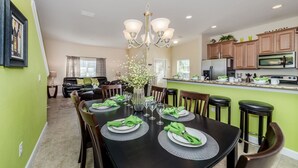 Comedor con una mesa negra dispuesta para seis personas, servilletas verdes y un jarrón con flores.