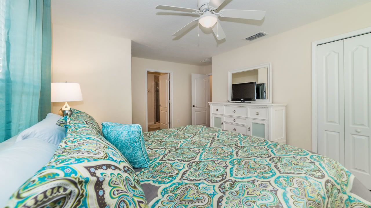 A bedroom with a bed, a dresser, a mirror, and a ceiling fan.