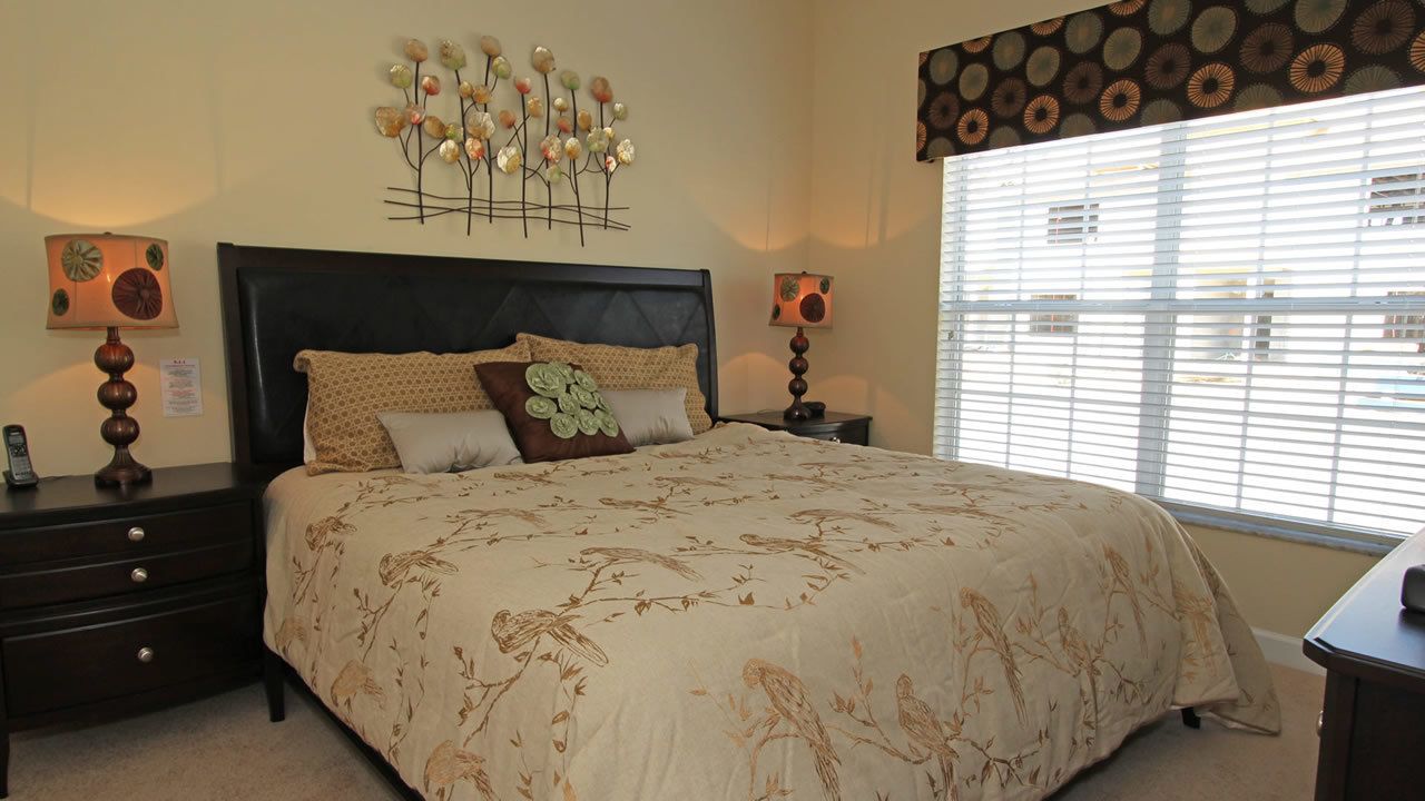 A bedroom with a large bed, two bedside tables, a wall-mounted lamp, and a window with blinds.