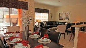 A dining area with a long table set for four, a black leather sofa, and a bar area. - Grhcal8974 - Paradise Palms Resort - 4 Bed 3 Baths Townhouse (Kissimmee)