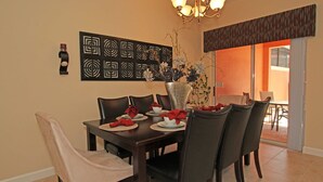 A dining area with a dark wooden table set for four, a vase with flowers, and a wall art piece. - Grhcal8974 - Paradise Palms Resort - 4 Bed 3 Baths Townhouse (Kissimmee)