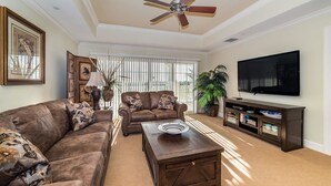 A living room with a brown leather sofa, a matching armchair, a wooden coffee table, a flat-screen TV, and a cabinet with decorative items. - Grhccr1368-302 - Reunion Resort - 3 Bed 3 Baths Townhouse (Kissimmee)