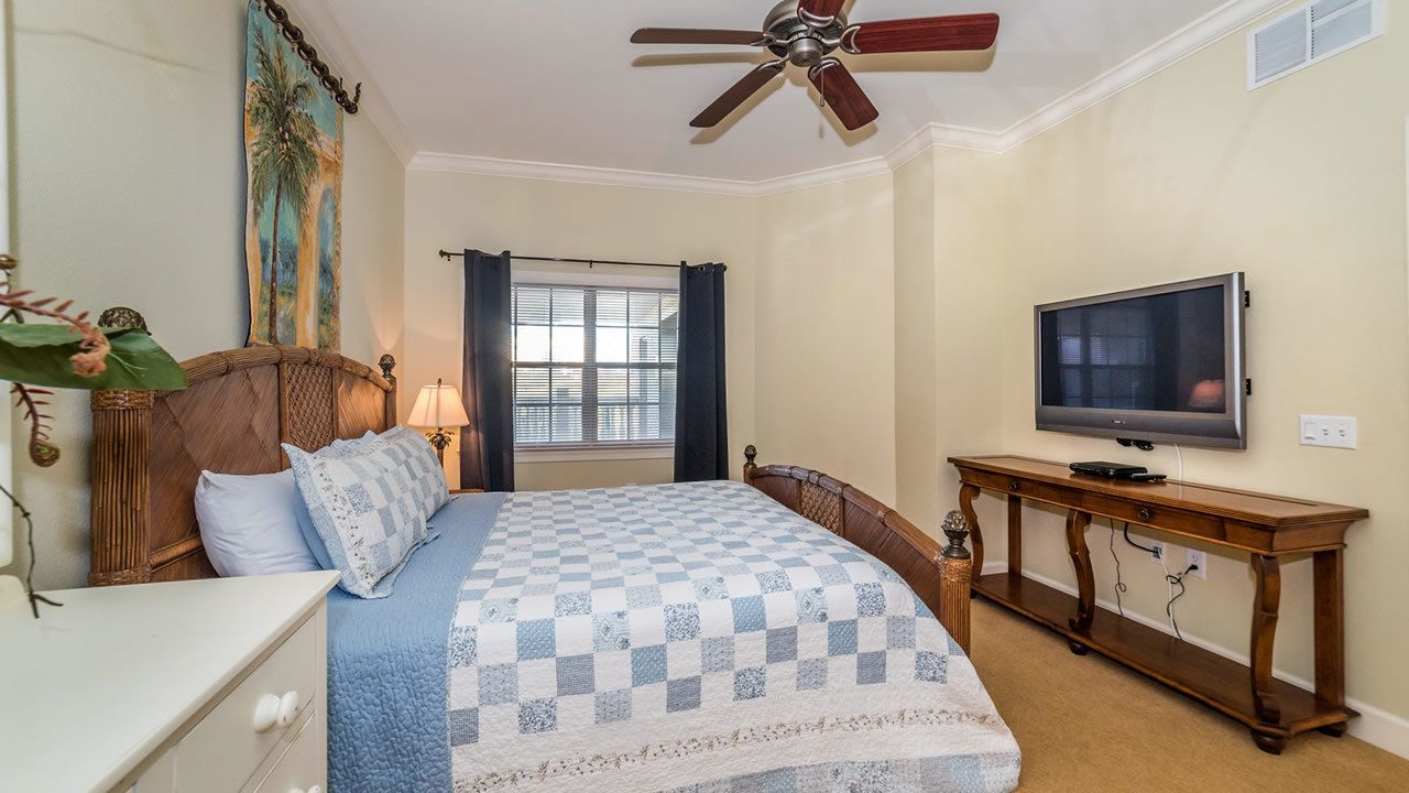 Ein Schlafzimmer mit Bett, Fernseher, Deckenventilator und einem Fenster mit Vorhängen.