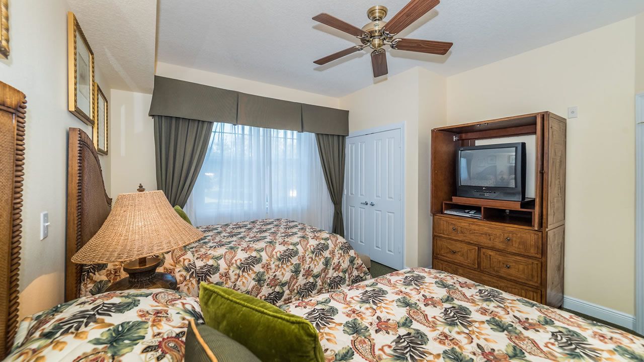 A hotel room with two beds, a ceiling fan, a television, and a wooden dresser.
