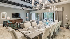 A spacious dining area with a large table set for a meal, a television mounted on the wall, and a ceiling fan.