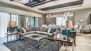 A modern living room with a leather sectional sofa, glass coffee table, and a dining area with a chandelier.