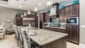 A modern kitchen with dark wood cabinets, stainless steel appliances, and a marble island.