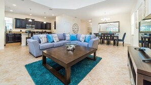 A spacious living room with a sectional sofa, a coffee table, and a dining area with a chandelier. - Grhbuc2995 - Paradise Palms Resort - 5 Bed 5 Baths House (Kissimmee)