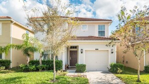 A two-story residential building with a white garage door, a front porch, and a small tree in the center. - Grhbuc2995 - Paradise Palms Resort - 5 Bed 5 Baths House (Kissimmee)