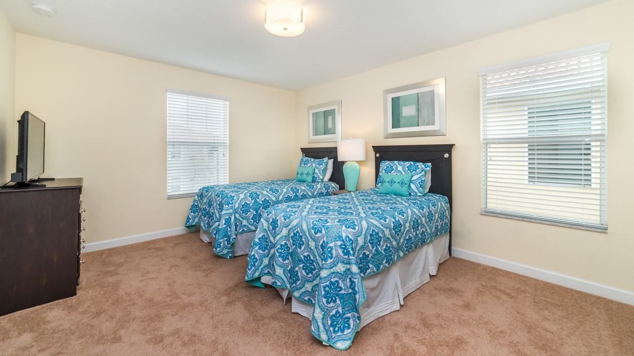 A bedroom with two beds, beige walls, and a carpeted floor.