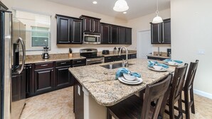 A modern kitchen with dark cabinetry, granite countertops, a central island with seating, and stainless steel appliances. - Grhbuc2995 - Paradise Palms Resort - 5 Bed 5 Baths House (Kissimmee)