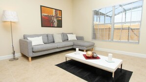 A modern living room with a grey sectional sofa, a white coffee table, a floor lamp, and a large window with blinds. - Grhbch3069 - Paradise Palms Resort - 4 Bed 3 Baths Townhouse (Kissimmee)