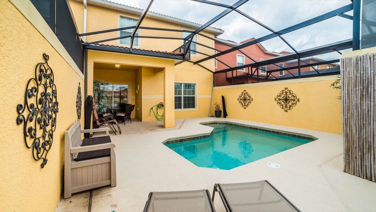 A backyard with a swimming pool, a covered patio, and a seating area with chairs and a table.