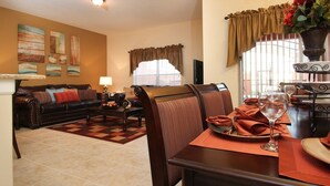 A living room with a sofa, coffee table, and dining table set with placemats and a wine glass. - Grhbch3081 - Paradise Palms Resort - 4 Bed 3 Baths Townhouse (Kissimmee)