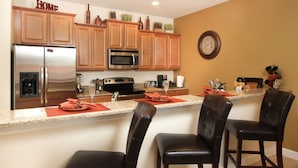 A kitchen with wooden cabinets, stainless steel appliances, and a bar area with two chairs. - Grhbch3081 - Paradise Palms Resort - 4 Bed 3 Baths Townhouse (Kissimmee)
