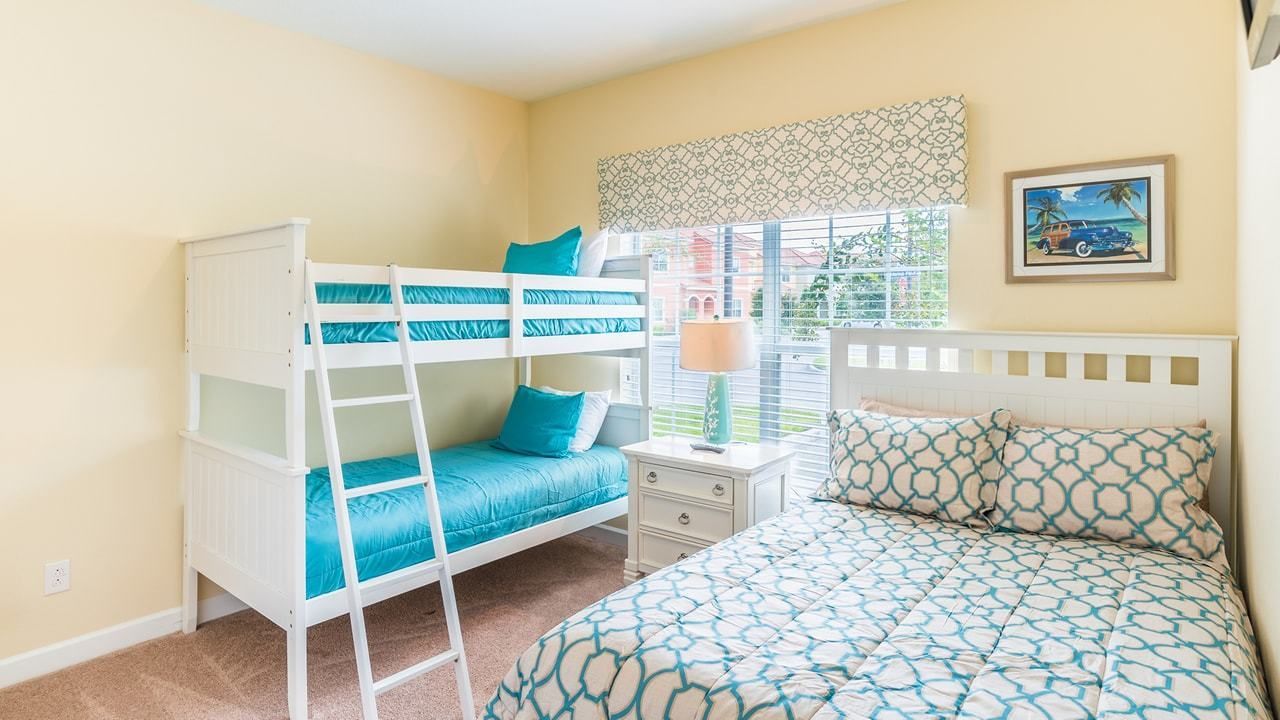 A room with bunk beds, a bedside table with a lamp, and a window with a view of greenery.