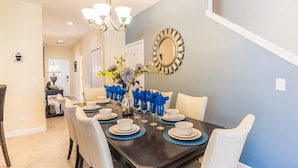 A dining room with a dark wooden table set for six, white chairs, and a vase with blue napkins. - Grhcal8951 - Paradise Palms Resort - 5 Bed 4 Baths Townhouse (Kissimmee)