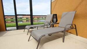 A sunroom with two lounge chairs and a table, large windows with a view of a lake and buildings.