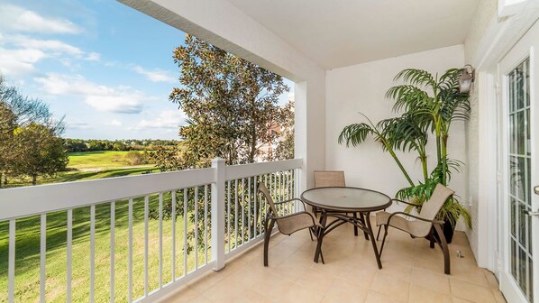 Un balcon donnant sur un terrain de golf, une table ronde avec des chaises et une plante en pot.