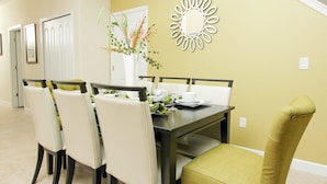 A dining area with a table set for four, surrounded by chairs, a decorative mirror, and a vase with flowers. - Grhmap8980 - Paradise Palms Resort - 5 Bed 4 Baths Townhouse (Kissimmee)