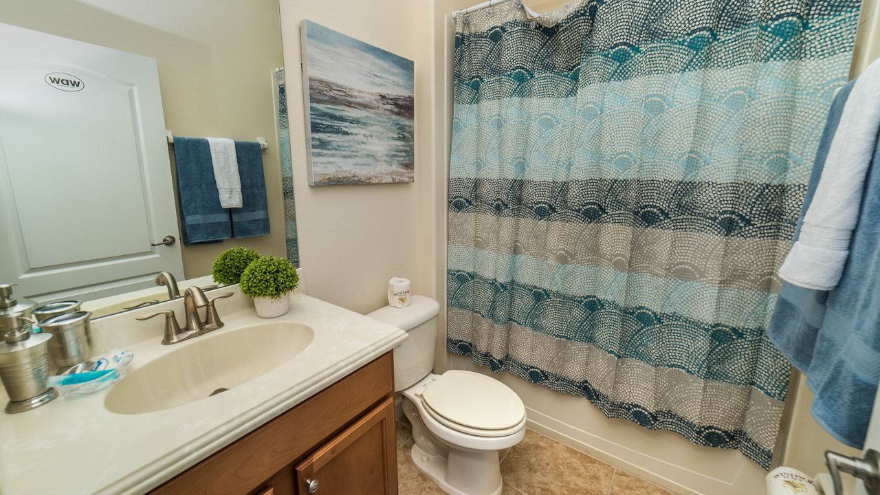 A bathroom with a double sink, a toilet, a shower curtain, and a towel rack.
